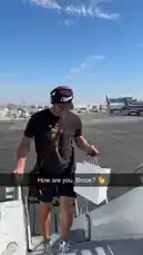 A man wearing LA Clippers gear disembarks from an airplane onto the tarmac under a clear blue sky. He carries a white paper bag and wears headphones, smiling as he walks down the stairs. by @clippers with Original Sound by clippers