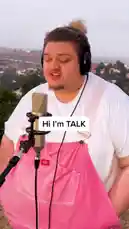 In this captivating performance, singer-songwriter TALK delivers a heartfelt cover of 'The World Is a Wild Place' in a stunning outdoor studio setting. Wearing a vibrant pink overall dress and white t-shirt, TALK sings passionately into a professional microphone while wearing headphones. The scenic hillside backdrop offers a beautiful contrast to the emotional intensity of the song. Text overlays reveal TALK's personal connection to the track, mentioning it was first heard on 'Grey's Anatomy'. This authentic, raw performance showcases TALK's powerful vocals and deep interpretation of the music. by @iamtalk with iamtalk by Contains: How To Save A Life - TALK