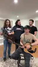 The AMH Band delivers a lively acoustic performance inside a bathroom. A young man sits on a stool playing a light-colored acoustic guitar while singing lead vocals. Behind him, three other band members provide backing vocals and harmonies; one plays a dark acoustic guitar, another wears a black 'MMA' t-shirt, and the third sings enthusiastically. They all perform together in sync, creating a fun and casual musical moment. by @amhbande with amhbande by Original Sound