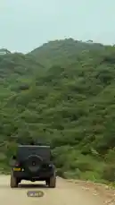 A black Jeep Wrangler drives along a dusty rural road, surrounded by dense green forests and rolling hills under a soft overcast sky. The vehicle moves steadily forward, showcasing scenic off-road exploration in a natural mountainous landscape. by @nowaira-11 with original sound
