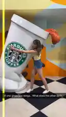 In a vibrant, surreal indoor setting, influencer Martine Beerman playfully interacts with a massive, tilted Starbucks coffee cup sculpture. Dressed in a yellow top and denim shorts, she leans against the oversized prop, creating a dynamic and humorous visual. The colorful background, checkered floor, and whimsical design suggest a modern art museum or themed attraction. As she pushes, the cup appears to be in motion, capturing a moment of lighthearted fun and creative expression. by @martine with Coffin Dance by Tony Production