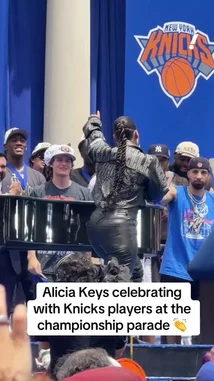 Singer Alicia Keys takes center stage during the New York Knicks' championship parade, performing and celebrating with the team. Dressed in a stylish black leather outfit, she interacts energetically with players wearing their championship hats and medals, all under a large 'New York Knicks' banner. by @yahoosports with Original Sound by yahoosports