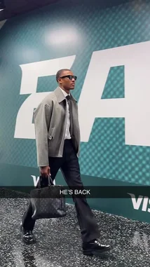 A man, identified as an Eagles player, confidently strides through a modern team facility hallway. He is dressed in a stylish grey jacket, black pants, and sunglasses, carrying a designer briefcase. The background features prominent green and white 'EAGLES' branding and 'VISA' logos, suggesting a professional sports environment. by @eagles with Original Sound by eagles
