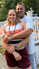 In this heartfelt scene, fitness influencer Mark The Shark embraces his partner outdoors after a workout. She wears a colorful sports tank top and maroon shorts, while he dons a white t-shirt and gray sweatpants. The couple shares a warm smile, highlighting their strong bond amidst a casual backyard setting with greenery and a white fence in the background. by @mts550 with original sound