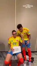 In this behind-the-scenes moment from the CONMEBOL Copa América 2024™, two Colombian footballers react to a fan's sign. One player, wearing jersey number 20, sits while holding a sign that reads '¡Vamos Quintero!' A teammate, wearing number 7, stands beside him, playfully interacting with the sign and making funny faces. The players are dressed in their official yellow and blue Colombia kits, creating a lighthearted and fun atmosphere. by @copaamerica with Original Sound by copaamerica