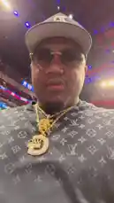 A man, identified as G-Mac Jazz, films himself at a Detroit Pistons game. He's wearing a Louis Vuitton shirt, a large gold chain with a 'G' pendant, and a black cap. He speaks to the camera before taking a drink from a white cup. The background shows the packed basketball arena and a large scoreboard. by @nbapistons with Original Sound by nbapistons