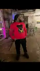 Watch Mayne showcase a bold streetwear look featuring a vibrant red sweatshirt with a black bear graphic and gold chain detail. Set against an industrial loft backdrop with ambient purple lighting, the scene captures a moment of urban style and confident presence. This authentic fashion moment is perfect for those interested in modern streetwear aesthetics. by @practiceneeded with original sound