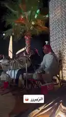Experience the vibrant atmosphere of a live Jalsah event under the night sky. This captivating performance features traditional Middle Eastern drummers, dressed in authentic white thobes and red-and-white ghutras, playing powerful rhythms on large tablas and other hand drums. The setting includes a beautifully lit palm tree and a patterned backdrop, creating an immersive cultural ambiance perfect for celebrations, weddings, or festive gatherings. by @jalsahevent with jalsahevent by Original Sound