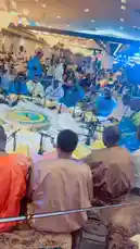 abdoufall205962 님이 만든 Original Sound 포함 @abdoufall205962 님이 만든 A large congregation gathers inside a grand mosque for a spiritual event led by Abdou Fall. Men dressed in traditional attire sit on prayer mats, attentively listening as he recites verses from the Quran. The ornate hall, illuminated by crystal chandeliers and vibrant blue stage lights, creates a solemn and reverent atmosphere.