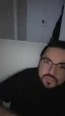 In this casual, selfie-style clip, David Valenz is seen sitting on a light-colored couch in a dimly lit room. He wears black-rimmed glasses and a black t-shirt, looking directly into the camera and making various playful facial expressions, including smiling and sticking out his tongue. by @mrvechain with Original Sound by mrvechain