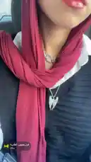 A close-up view of Hana showcasing her stylish outfit, featuring a vibrant red scarf elegantly draped around her neck, layered over a crisp white collared shirt and a dark textured sweater. She accessorizes with two distinct silver-toned necklaces: one with a delicate wing design and another with a larger, sparkling heart-shaped pendant. The scene captures a moment of personal style and fashion-forward presentation. by @inxhell with فين حبيب القلب؟ by Contains: Helwa Ya Baladi - JadaL