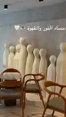 This video offers a stylish glimpse into Sequence Coffee, showcasing its minimalist interior design. Viewers see modern wooden chairs arranged around a small table, set against a striking wall installation of white, abstract humanoid sculptures. The aesthetic is clean and contemporary, emphasizing art and comfort. Text overlay in Arabic reads 'مساء النور والقهوة' (Good evening, light, and coffee), adding a warm, inviting tone. This scene highlights the café's unique ambiance, perfect for casual meetings or quiet relaxation. by @sequence-coffee with original sound