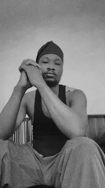 A black-and-white, cinematic portrait of artist Semi. He sits in contemplative stillness, hands clasped under his chin, wearing a beanie and tank top. The minimalist composition focuses entirely on his expression and presence, creating an intimate and powerful moment. by @ralphsemi with Many People by Adekunle Gold