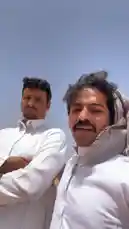 This video features مناحي الرجباني and a companion in traditional white attire, standing against a vast desert backdrop under a clear blue sky. They are seen observing their surroundings, which include expansive sandy terrain and a distant waterway. The scene captures the serene yet rugged beauty of the arid environment. by @manahi.20 with manahi.20 by Original Sound