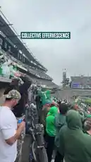 In a packed stadium under an overcast sky, Philadelphia Eagles fans erupt in celebration after a touchdown. Dressed predominantly in green, they wave flags, cheer, and launch smoke flares into the air, creating a powerful 'collective effervescence' of team spirit. by @eagles with Original Sound by eagles
