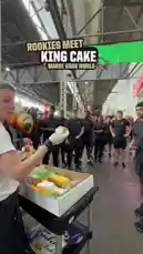 In a festive behind-the-scenes look at Mardi Gras preparations, a group of New Orleans Saints players gather to celebrate the tradition of receiving the King Cake. A woman hands out slices of the colorful cake to the team members, including rookie Jeremiah Wright, who proudly displays his slice after finding the hidden plastic baby inside. The moment is captured with humor and camaraderie, showcasing a beloved cultural ritual before the team's big game. by @saints with Original Sound by saints