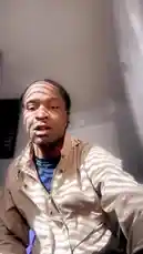 In this direct-to-camera vlog, Da First Option ⚡️ sits in his room and discusses his current style. He's wearing a beige jacket over a blue shirt and has braided hair. Sunlight streams through blinds, casting distinct shadows across his face and clothing. He uses expressive hand gestures while speaking, creating a casual and engaging atmosphere. by @nascarfeezy with Original Sound by nascarfeezy