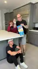 In a modern kitchen, three men participate in a comedic prank involving Ruffles potato chips and Corona beer. A bald man in a black shirt dramatically shakes a bag of chips over a bottle, causing a messy spill onto the counter and the other man's hoodie. The scene captures their exaggerated reactions and playful interaction, showcasing THE MAGIC CRASHER's signature style of lighthearted, physical humor. by @themagiccrasher with Original Sound by themagiccrasher
