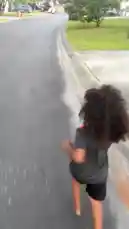A young child with long, curly hair runs barefoot down a wet asphalt road, their feet splashing through puddles. The camera follows from behind as they run along the edge of the pavement next to a grassy area. The sound of rhythmic footsteps on the damp surface creates a playful and energetic atmosphere. by @marcus.randall with Original Sound by marcus.randall