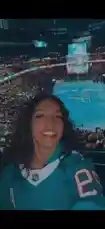In this vibrant scene, Sasha takes a selfie amidst the lively atmosphere of a packed hockey arena during an NHL game. She's dressed in a teal jersey, smiling brightly as she enjoys the electric energy of the crowd and the illuminated ice rink below. The camera pans across the bustling stadium, showcasing fans cheering and the large jumbotron displaying live action, creating an immersive fan experience. by @squashha with squashha by Original Sound