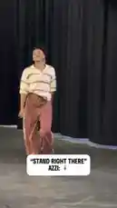 A woman, identified by on-screen text as 'AZZI:', walks confidently across a stage-like area with black curtains. She is wearing a beige and brown striped polo shirt, wide-leg rust-colored pants with a side stripe, and white sneakers. She smiles and poses for the camera before turning and walking away. by @wnba with Original Sound by wnba