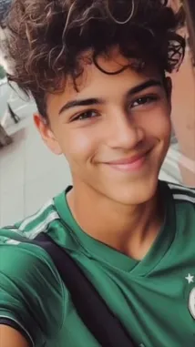This short clip features Mexican social media personality Nico Arellano Ortiz filming himself in a selfie-style video on a city sidewalk. He is wearing a green Mexico national team soccer jersey and smiles warmly at the camera, occasionally adjusting his curly hair. The background shows a typical urban street with buildings and trees. Text overlays display his username '@jalisco6061919' and full name 'Nico Arellano Ortiz'. The overall vibe is casual and friendly, capturing a moment of his day. by @jalisco6061919 with original sound
