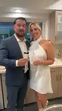 오리지널 사운드 포함 @itsma_bitchezz 님이 만든 In this stylish snapshot, Diana V is seen enjoying a celebratory evening with a partner in a modern kitchen setting. She wears a chic white one-shoulder mini dress, complemented by elegant white heels and gold accessories. Her companion is dressed in a sharp navy suit with a playful bowtie-shaped charm on his champagne flute. Both hold glasses of bubbly, smiling warmly at the camera, capturing a joyful moment perfect for social sharing.