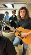 This behind-the-scenes look at the AMH Band shows four musicians rehearsing together in a studio. One member takes center stage, playfully interacting with the camera while his bandmates provide musical accompaniment on acoustic guitars. The atmosphere is relaxed and full of energy, capturing the camaraderie and fun of creating music as a group. by @amhbande with amhbande by Original Sound