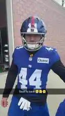A close-up shot captures a New York Giants football player wearing his full uniform and helmet, smiling at the camera in what appears to be a locker room or tunnel area before a game. Another team member is visible in the background. by @newyorkgiants with newyorkgiants by Original Sound