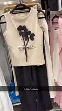 A close-up showcase of a trendy sleeveless top featuring black floral appliqués and a motivational quote, paired with sleek black pants. This outfit is part of a curated collection from كود اناقتي, highlighting modern women's fashion styles perfect for casual outings or stylish everyday wear. by @code.a3 with original sound