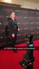 A man poses confidently on a red carpet in front of a 'CHESS' branded backdrop during what appears to be a promotional event for Chess.com. He adjusts his suit jacket before striking various poses for the camera. by @chesscom with Original Sound by chesscom