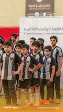 This video captures the Al-Shabab Club Academy Tournament for Youth categories, showcasing young athletes proudly standing in formation before their competition. The players wear matching black-and-white striped jerseys and dark shorts, representing their team spirit and dedication. In the background, banners display Arabic text identifying the event and its sponsors, including 'جمعية اللاعب' (The Players Association). The atmosphere is one of anticipation and pride, highlighting youth development and community engagement in football. by @playerassoc with original sound