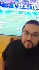 In this festive and energetic scene, David Valenz shares his holiday spirit while watching a live sports game on TV. Dressed casually in a black shirt, he holds a beverage and engages with the camera, smiling and reacting to the action on screen. A beautifully decorated Christmas tree with lights and ornaments stands beside him, creating a warm and joyful atmosphere. The television displays a football player celebrating a touchdown, adding excitement to the moment. This blend of personal celebration and shared sporting excitement captures a perfect holiday evening. by @mrvechain with Original Sound by mrvechain