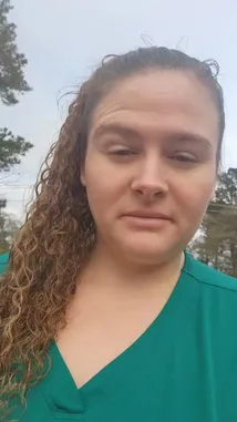 A close-up shot of Britny from 'Off the Map Travel' speaking directly to the camera while outdoors. She is wearing green scrubs and has curly hair tied back. The background features trees and houses under an overcast sky, suggesting she might be sharing travel tips or personal experiences during her journey. by @daisy.mae21 with daisy.mae21 by Original Sound