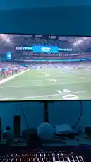 This video showcases a live NFL game broadcast on a large monitor within a personal gaming setup. The footage captures key moments from a Detroit Lions vs. Dallas Cowboys matchup at Ford Field, including a player returning a kickoff and a defensive tackle. The scene transitions to show the viewer's desk environment, featuring a keyboard, mouse, and various accessories, providing a behind-the-scenes look at a fan's game night experience. by @mrvechain with Original Sound by mrvechain