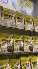 This video provides a detailed, close-up view of LA Nutrition's Whey Protein Complex products displayed on a retail shelf. The camera pans across multiple packages, highlighting the '100% WHEY PROTEIN COMPLEX' branding, nutritional information like 'PROTEIN 26g', and various flavor options including chocolate and vanilla. The consistent packaging design and prominent placement suggest a focus on product visibility and consumer choice. by @lanutritioniraq with original sound