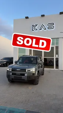 A sleek, modern KAS SUV is showcased in front of a dealership, with a prominent 'SOLD' graphic overlaying the scene. The vehicle is parked on a brick-patterned lot under a clear sky, highlighting its design and appeal. by @aaaaaa with كاريزما عاليه by '