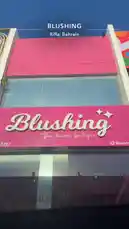 A bright pink storefront for 'Blushing The charm boutique' in Riffa, Bahrain, stands out against a clear blue sky. The modern building features large glass windows and prominent signage, showcasing a chic and inviting retail space. by @bx301a with baby baby baby 🫦🫦🫦🫦🫦 by @kauthareria