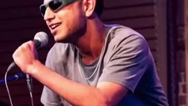 This high-energy performance features K-DEV, a charismatic singer wearing a gray t-shirt and distinctive green-framed sunglasses. He passionately sings into a microphone, his expressive face and dynamic posture conveying deep emotion and connection with the music. The intimate setting, likely a small concert or open mic night, highlights his raw talent and stage presence. by @k_dev170 with Original Sound by k_dev170