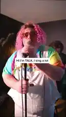 Witness TALK delivering a passionate live performance in a cozy music venue. Dressed in a colorful tie-dye shirt and white overalls, they sing into a microphone while a guitarist plays in the background. The atmosphere is intimate and energetic, capturing the essence of a live band act. by @iamtalk with iamtalk by Original Sound