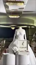 A beautifully styled wedding display features a stunning white bridal gown on a mannequin, accompanied by a bouquet, perfume bottles, and a decorative calendar for August 2026. The setting is a luxurious event hall with ornate gold chairs and crystal chandeliers, creating an atmosphere of sophistication and celebration. by @me_ha73 with Original Sound by me_ha73
