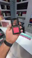 This quick beauty tutorial from بوتيك ماريا demonstrates the proper technique for applying blush using a compact powder blush. The video shows a hand swatching the vibrant pink color on the back of the hand to display its true pigmentation and finish, providing viewers with a clear visual guide. by @butik.mariya with شون منظر😂 by 😂
