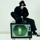 In this static scene, artist Jez Dior sits atop a retro television set against a stark white tiled wall. He wears a black hoodie and dark pants, with a visible tattoo on his hand. The TV screen glows green, displaying a glowing coffin icon with rays emanating from it. The image conveys a moody, artistic aesthetic often associated with modern music artists and alternative fashion. by @jezdior with original sound