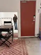 In this exclusive behind-the-scenes look, fashion influencer Jez Dior shares a candid moment from their personal space. The scene captures Jez taking a mirror selfie in a stylishly decorated room featuring a red door, a vintage makeup vanity with lights, and a cozy patterned rug. This intimate setting reveals the blend of fashion, personality, and creativity that defines Jez Dior's unique aesthetic. by @jezdior with original sound