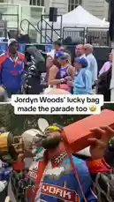 In this celebratory moment from the New York Knicks championship parade, fans and players share in the joy. The top half of the screen shows a woman in a 'Knicks 32' jersey, who is later revealed to be Jordyn Woods, embracing another fan. The bottom half features a player holding a giant orange lucky bag, humorously referencing the woman's distinctive handbag. This split-screen view captures the fun and excitement of the event. by @yahoosports with Original Sound by Contains: bologna 2 - boolymon