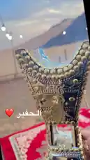 A close-up view of a beautifully ornate incense burner, intricately decorated with gold studs and filigree, sits atop a red patterned cloth against a scenic desert backdrop. The camera slowly pans around the object, highlighting its craftsmanship and the serene atmosphere of the outdoor location. by @nouf4445 with nouf4445 by Original Sound