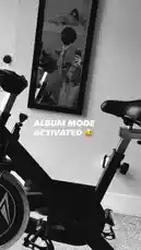 A black-and-white, static shot captures Jez Dior mid-workout on an exercise bike, with a mirror reflecting their energetic pose. Text overlay 'ALBUM MODE ACTIVATED' adds a playful, creative flair, suggesting a moment of personal expression during fitness. This still image conveys a blend of lifestyle, motivation, and digital culture. by @jezdior with original sound