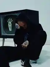 A person with extensive tattoos sits in a black hoodie against a stark white wall, head bowed in contemplation. Behind them, a vintage television displays a glowing neon coffin symbol. The scene is moody and stylized, evoking themes of introspection and modern street culture. This powerful visual is associated with artist Jez Dior. by @jezdior with original sound