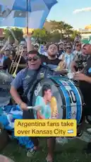 A vibrant crowd of Argentina supporters takes over a park in Kansas City, celebrating their team's victory with music, flags, and festive energy. The scene is filled with fans wearing national colors, playing drums featuring Lionel Messi, and waving the Argentinian flag under the sun. by @yahoosports with Original Sound by yahoosports