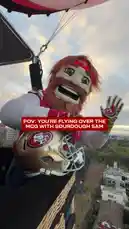 A person in the Sourdough Sam mascot costume enjoys a scenic hot air balloon ride over Melbourne, Australia. The flight offers breathtaking views of the city skyline, other balloons in the air, and provides a clear sightline of the Melbourne Cricket Ground (MCG). The footage captures the excitement of the experience, culminating in a promotional message for an upcoming event. by @sf49ers with Original Sound by sf49ers